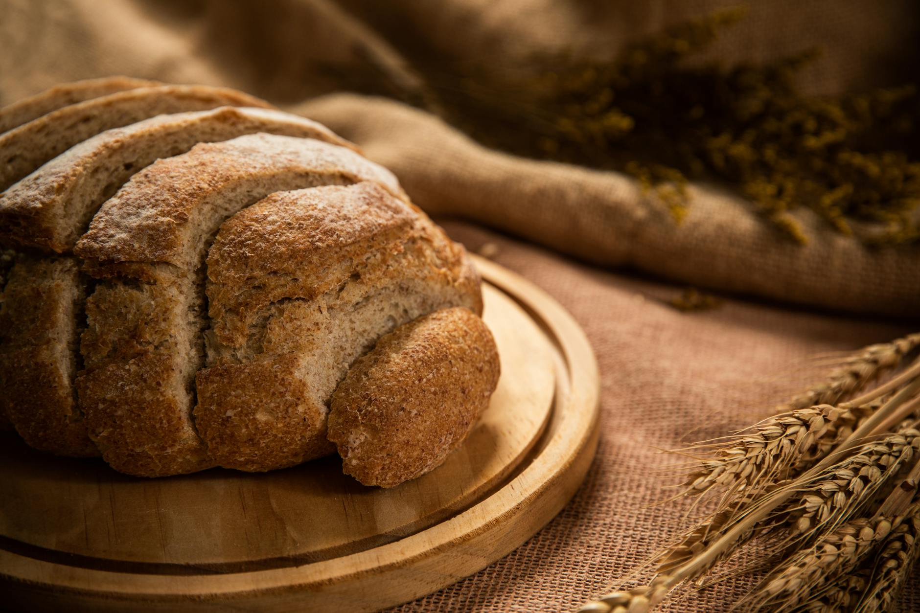Bochenek domowego chleba pełnoziarnistego na desce z kłosami pszenicy