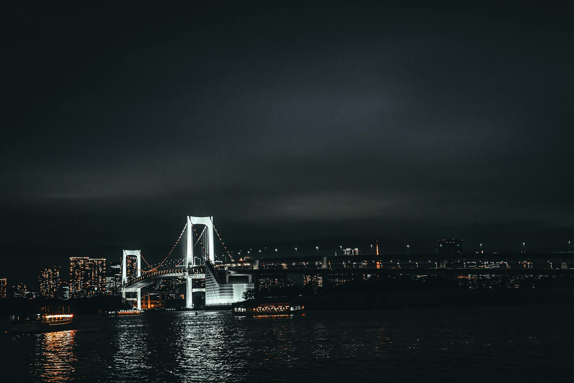 Nocny widok na Rainbow Bridge w Tokio odbijający światła miasta w wodzie