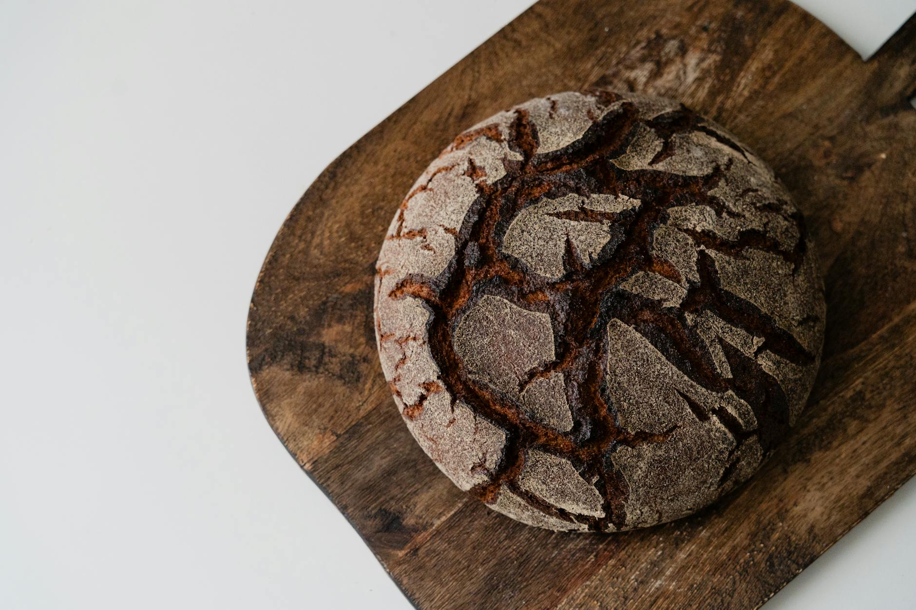 Okrągły, rustykalny bochenek chleba pełnoziarnistego na desce