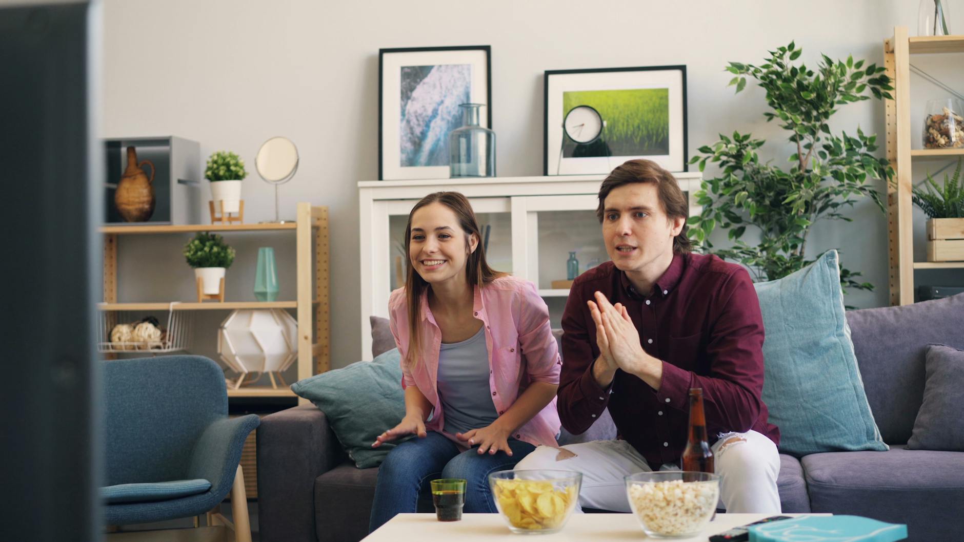 Para ogląda z ekscytacją anime w salonie, jedząc przekąski