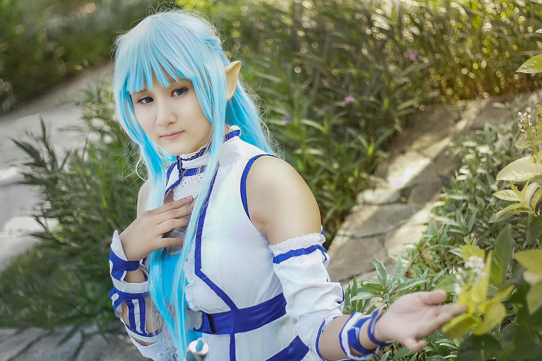 Cosplayerka z niebieskimi włosami pozuje w zielonym ogrodzie