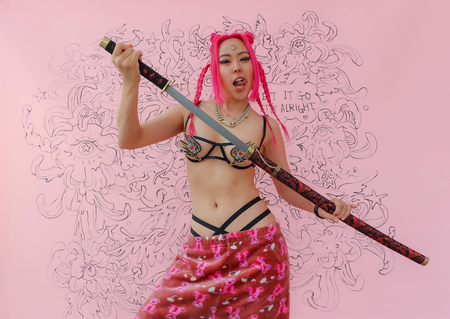 Cosplayerka z różowymi włosami pozuje z kataną na różowym tle