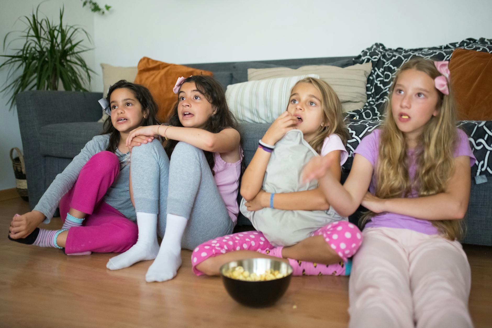 Cztery dziewczyny w piżamach oglądają film i jedzą popcorn na podłodze