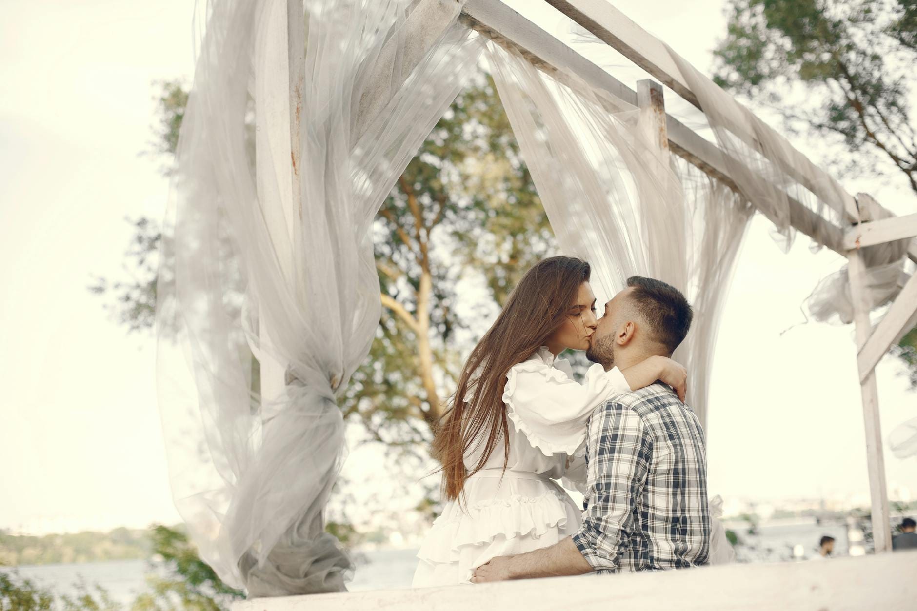 Para całująca się pod białą altaną w spokojnym plenerze