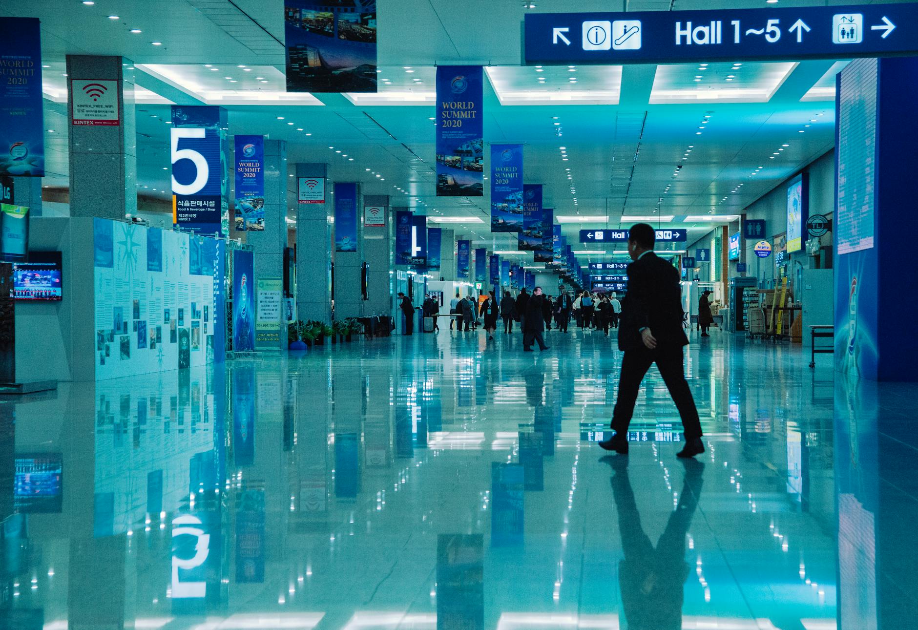 Tłum ludzi w jasnej hali konferencyjnej z tablicami kierunkowymi