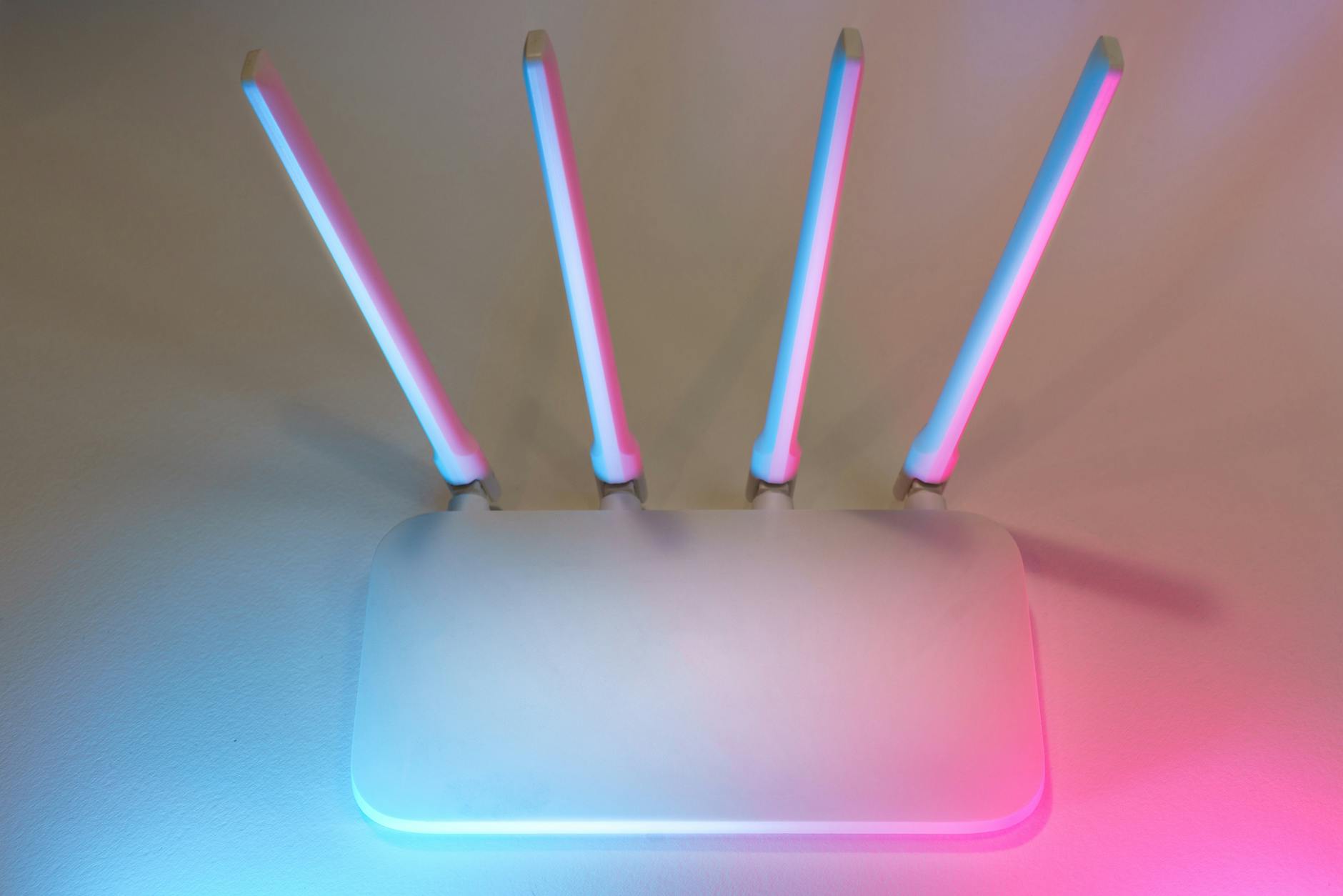 Jak skutecznie zabezpieczyć domową sieć Wi‑Fi: praktyczny poradnik dla użytkowników komputerów Biały router Wi‑Fi z czterema antenami w niebiesko‑różowym świetle