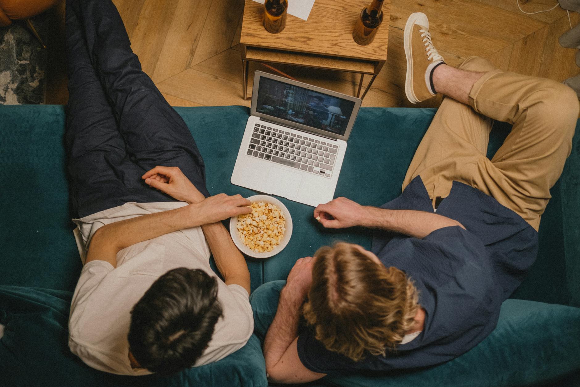 Dwóch znajomych ogląda anime na laptopie, jedząc popcorn na kanapie