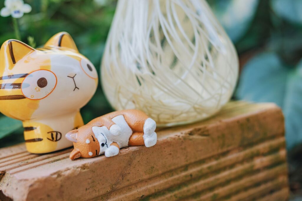 Ceramiczne figurki kotów na ceglanej powierzchni z zielonym tłem